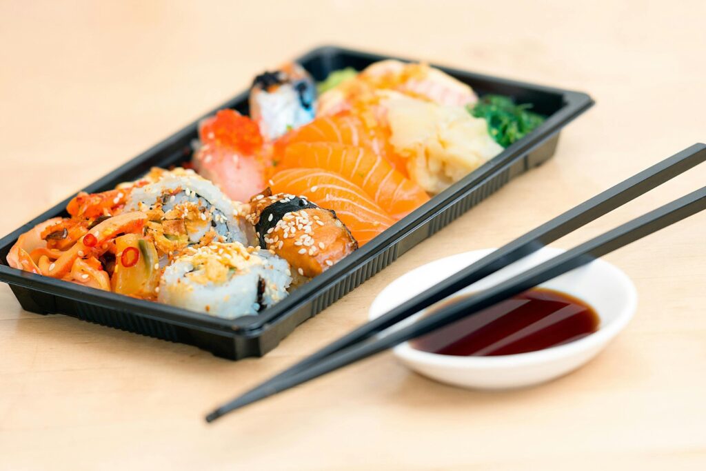 A platter of multiple kinds of sushi laid with different seasonings accompanied with its sauce and chopsticks.