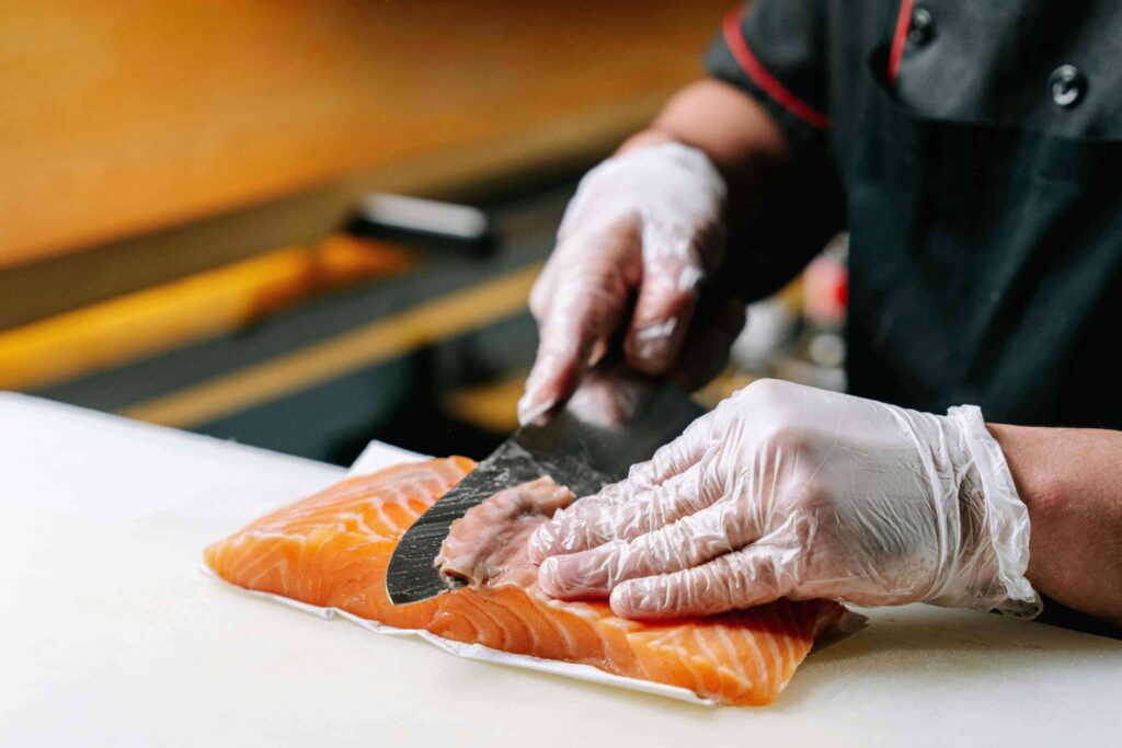 A sushi chef demonstrating the level of attention in slicing salmon to prepare for sushi.