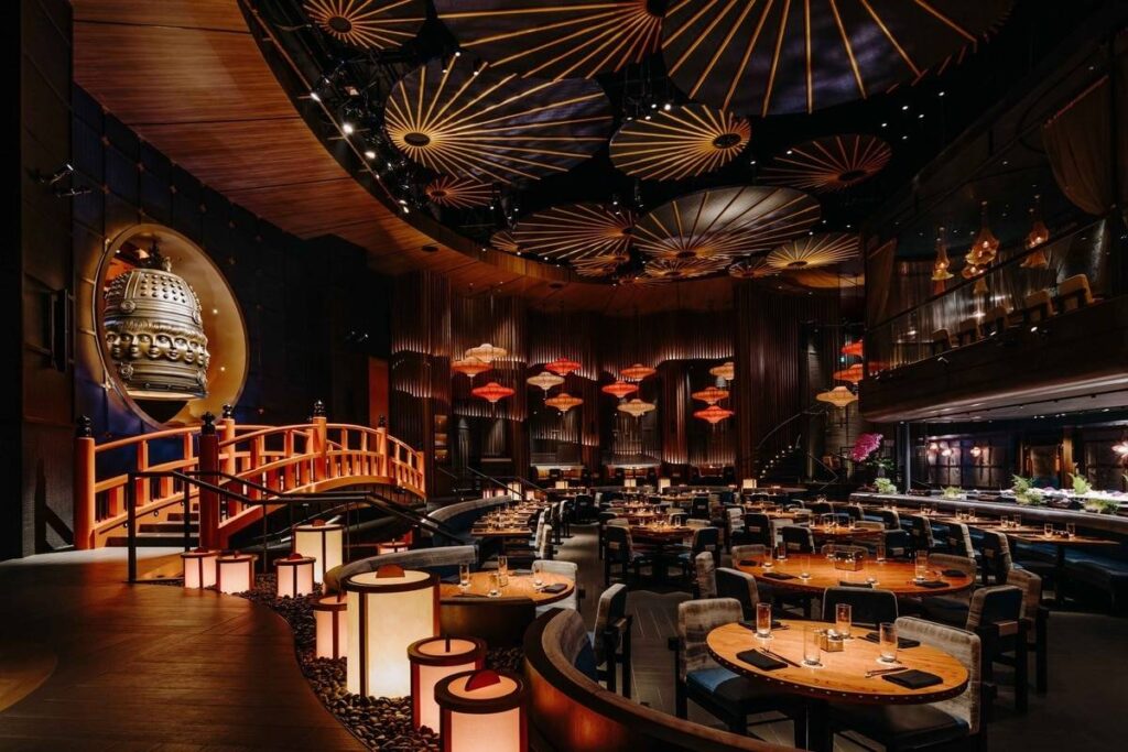 Overhead view of a full Japanese dining spread featuring various dishes: maki rolls, sashimi, yakitori skewers, gyoza dumplings, onigiri rice balls, and miso soup.