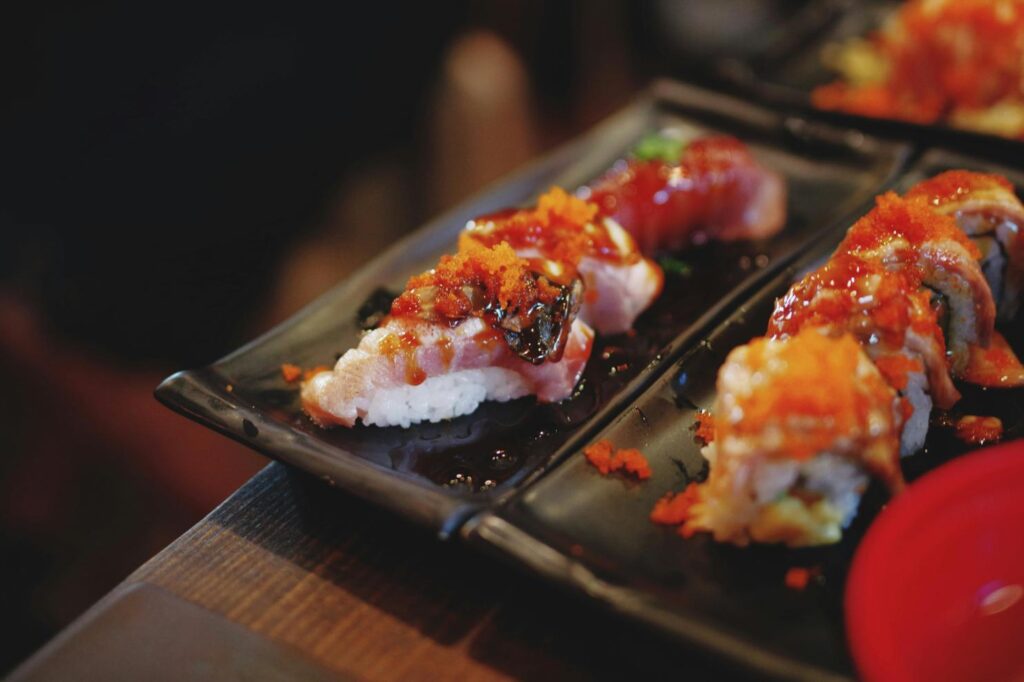 A photo of a maki sushi placed on a black rectangular plate while sitting on a dark wooden table.