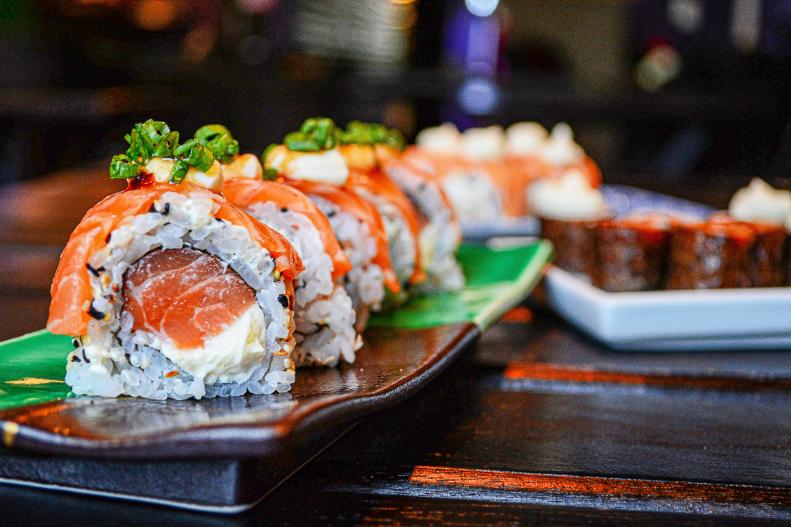 A platter of sushi laid aesthetically slanted to one another above a brown decorative platter.