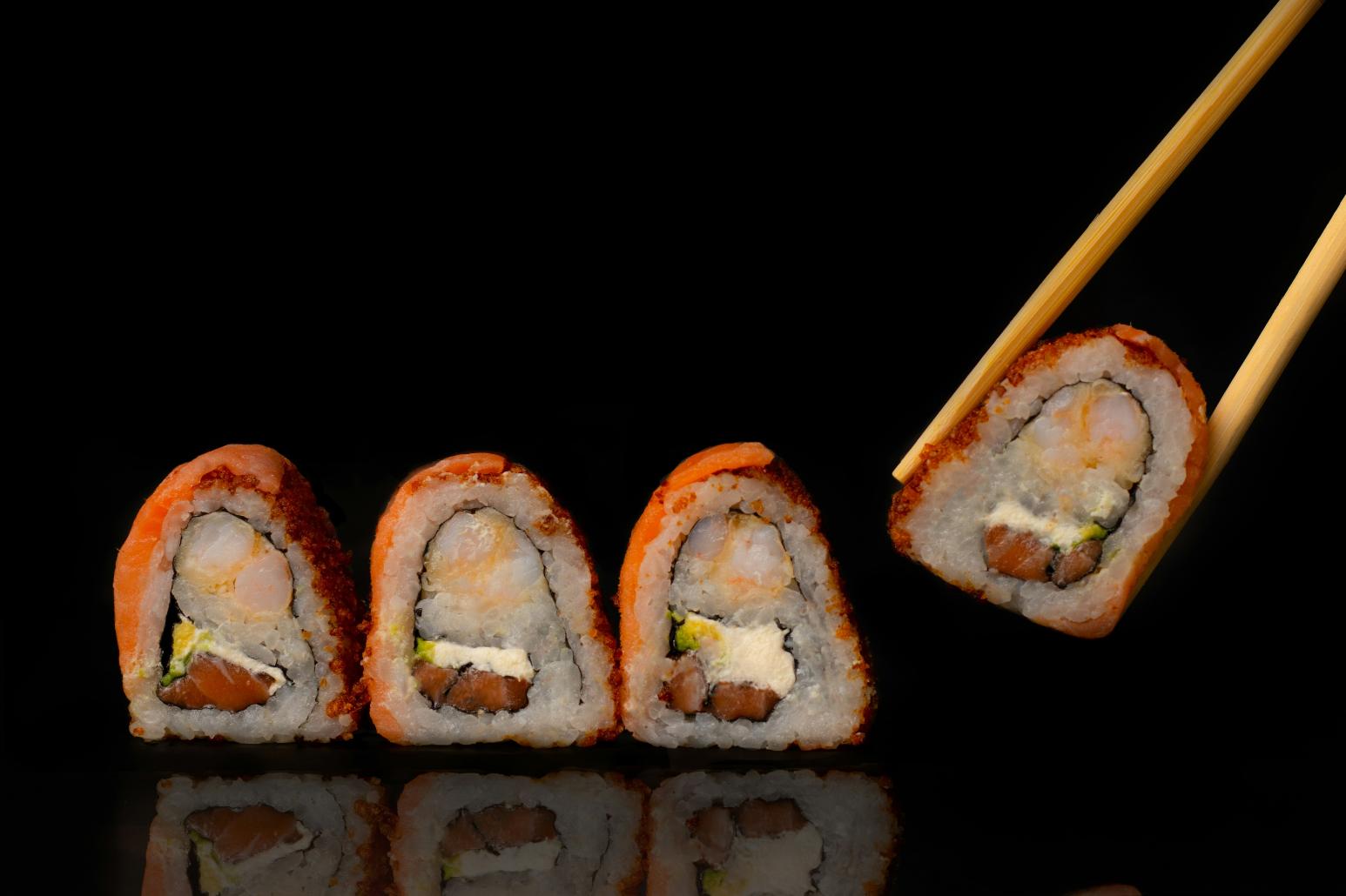 Four pieces of sushi alongside one another with the right most sushi on a chopstick against a black background.
