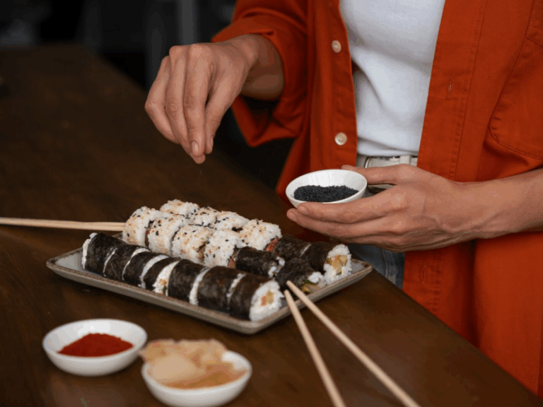 A high-end plate of sushi being prepared with black sesame seeds.