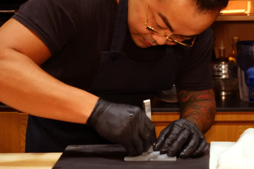 Chef preparing sushi at omakase counter.