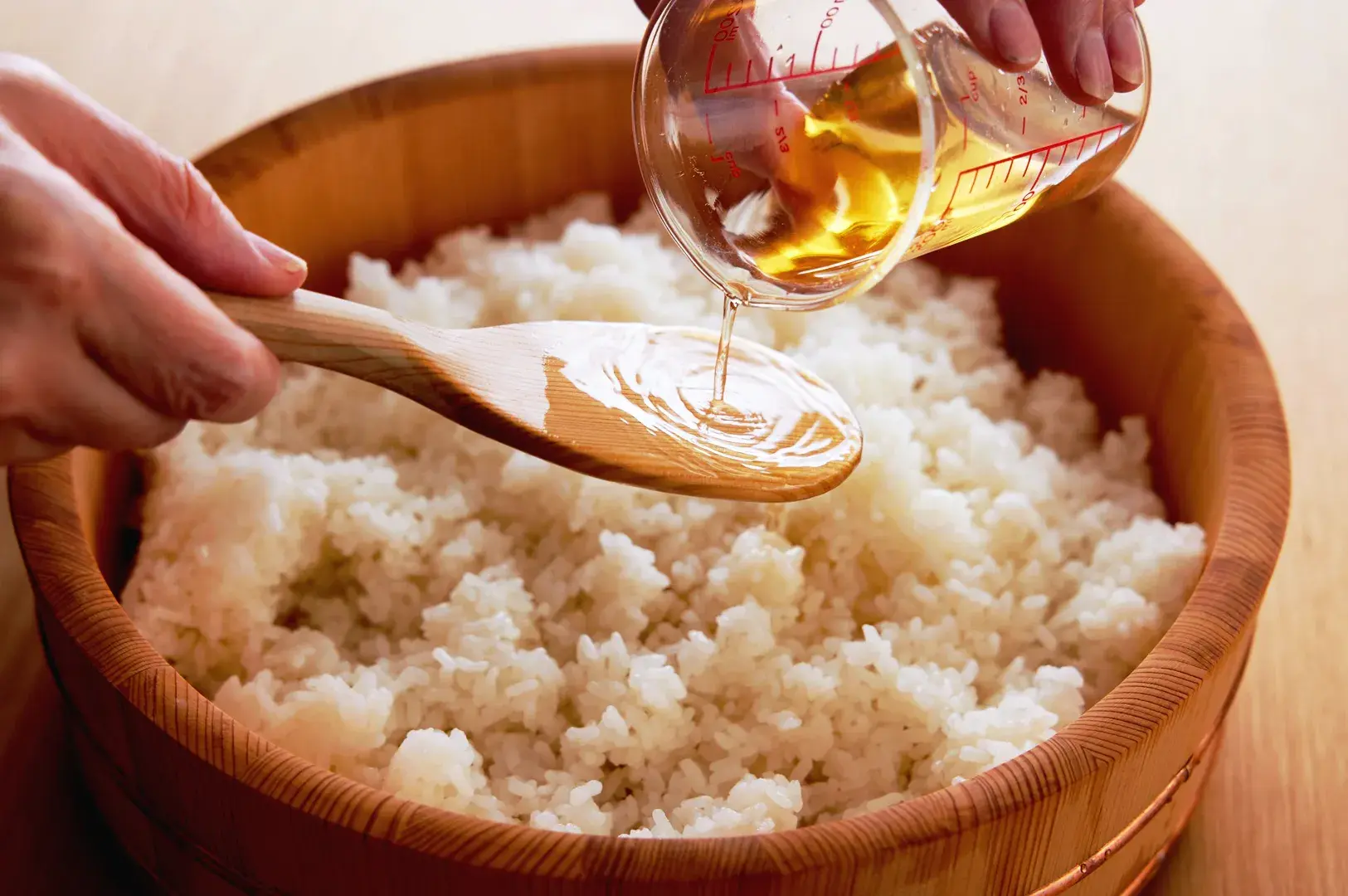 Sushi rice being seasoned with vinegar in a traditional wooden hangiri bowl
