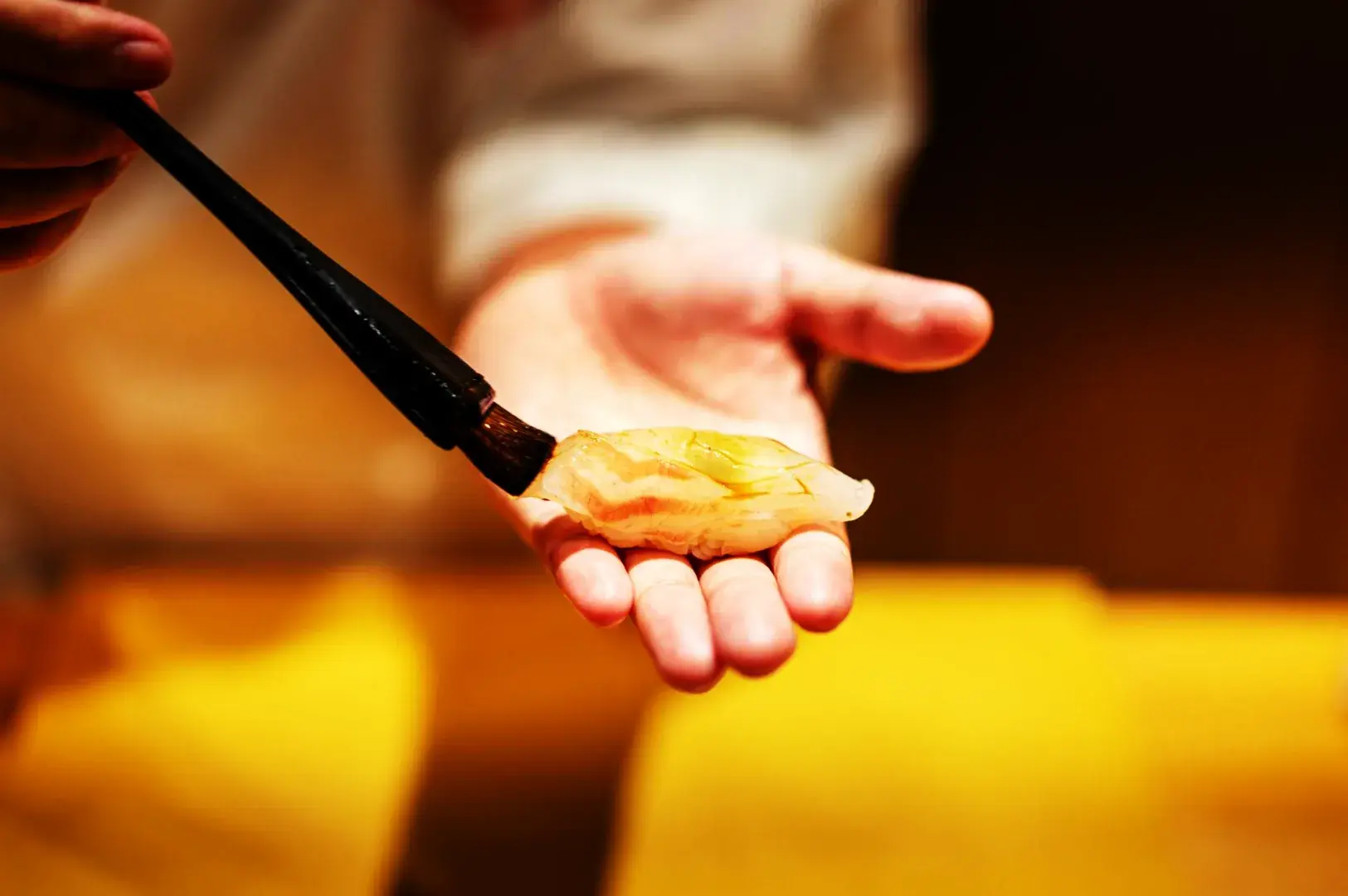 Sushi chef brushing sauce onto nigiri by hand in an omakase setting