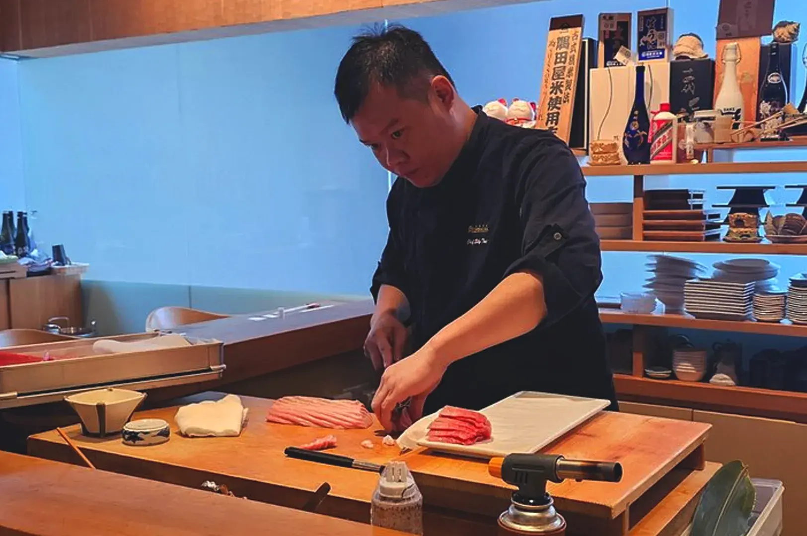 Chef at Standing Sushi Bar Singapore preparing fresh salmon sashimi with precise knife technique in a casual restaurant setting