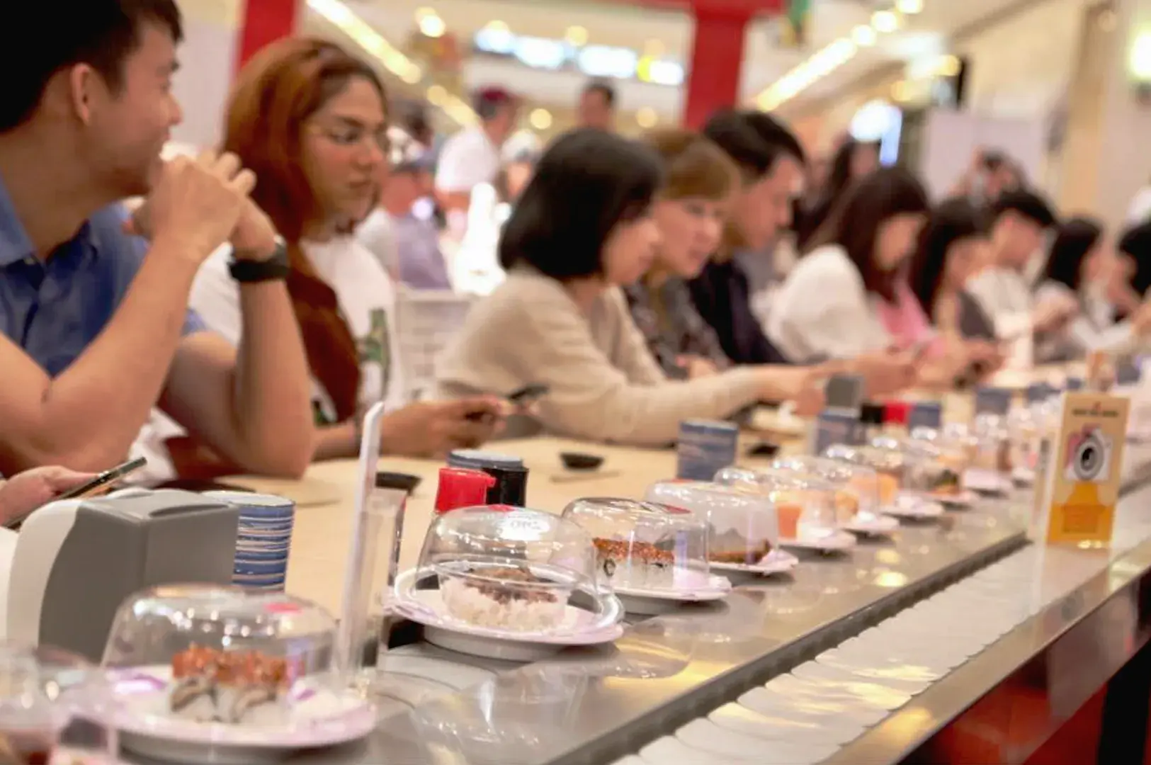 Conveyor belt sushi restaurant in Singapore with diners selecting affordable sushi plates, highlighting kaiten sushi and accessible Japanese dining