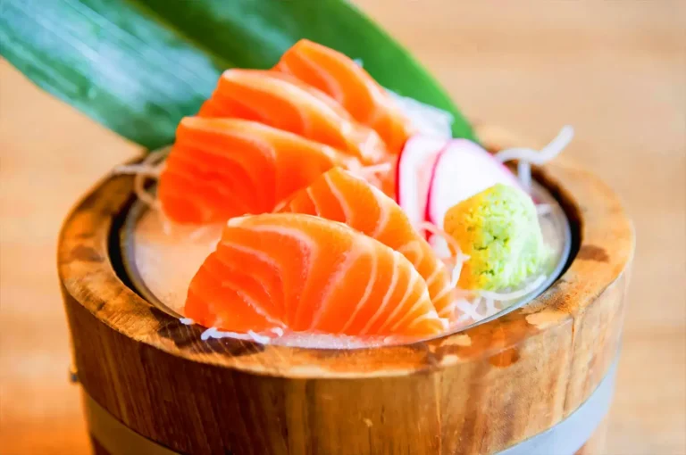 Fresh salmon sashimi served over ice in a traditional wooden bowl with wasabi and radish, showcasing premium Japanese seafood dining in Singapore