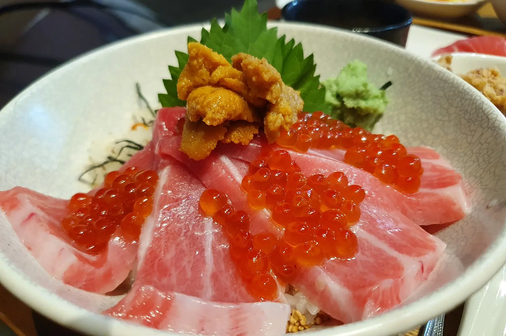 Tuna sashimi bowl topped with salmon roe, sea urchin, and shiso leaf garnish