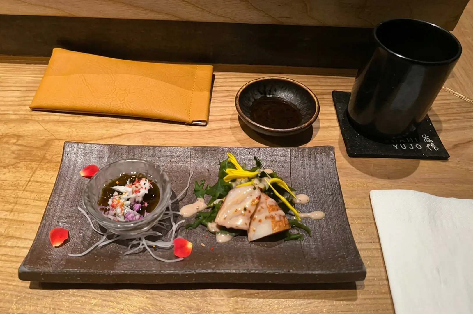 Grilled fish and tartare on dark ceramic plate at omakase counter