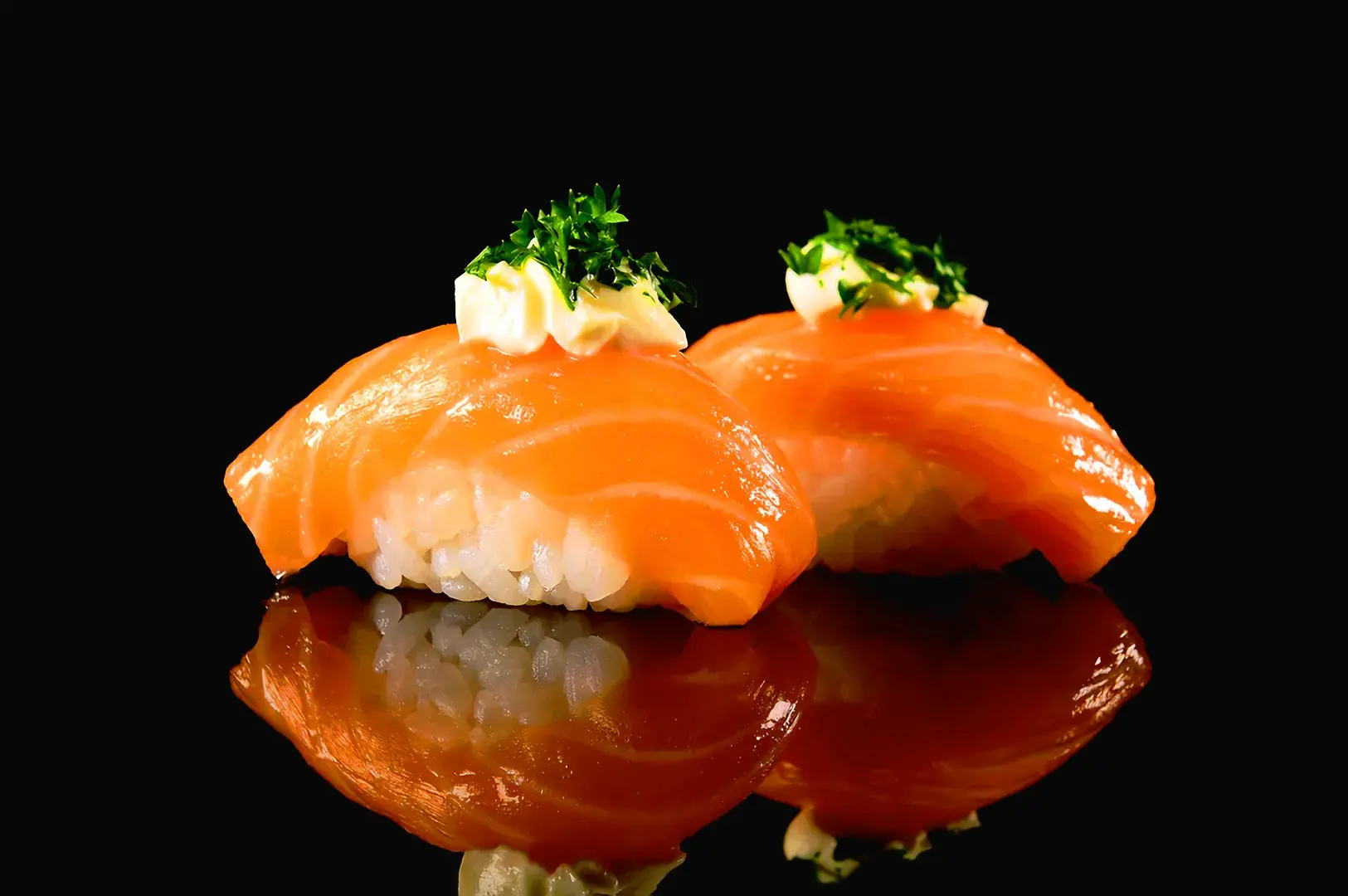 Salmon nigiri sushi topped with creamy sauce and herbs on a black reflective surface, featuring modern Japanese sushi presentation in Singapore dining scene