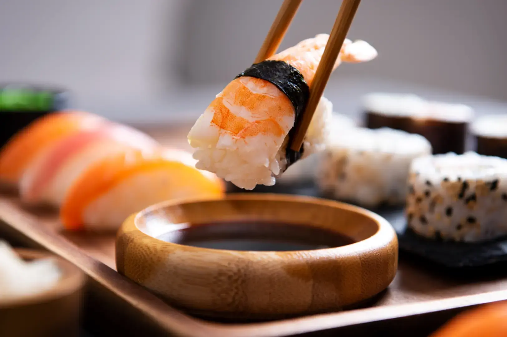 Chopsticks holding a nigiri above soy sauce