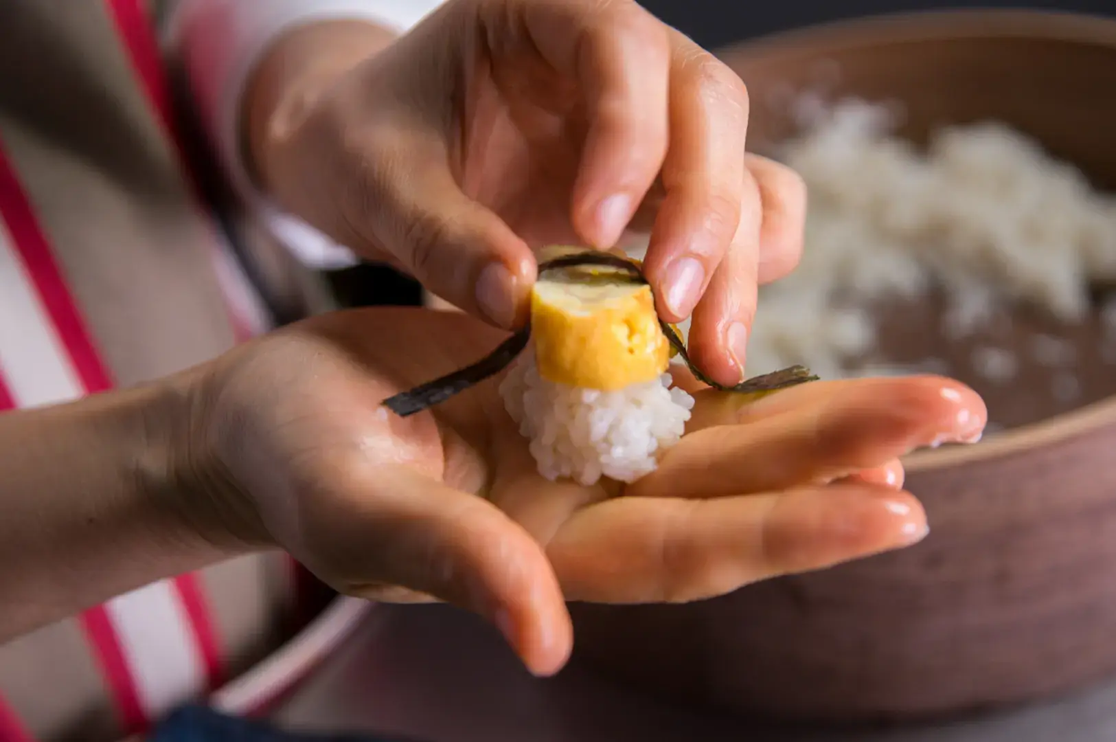 Hands shaping nigiri with tamago and nori