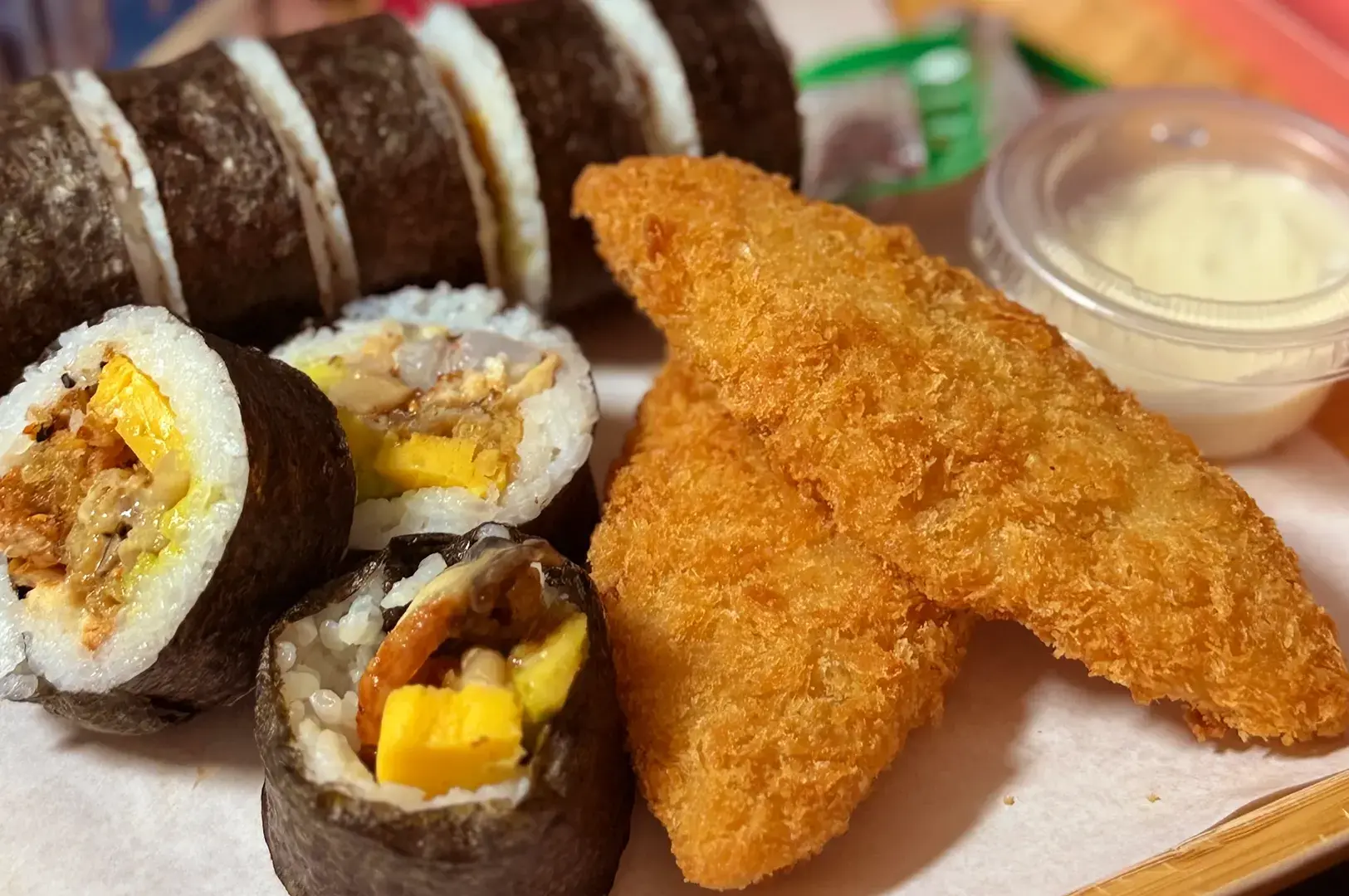 Sushi rolls with breaded fried pieces and a dipping sauce on a tray.