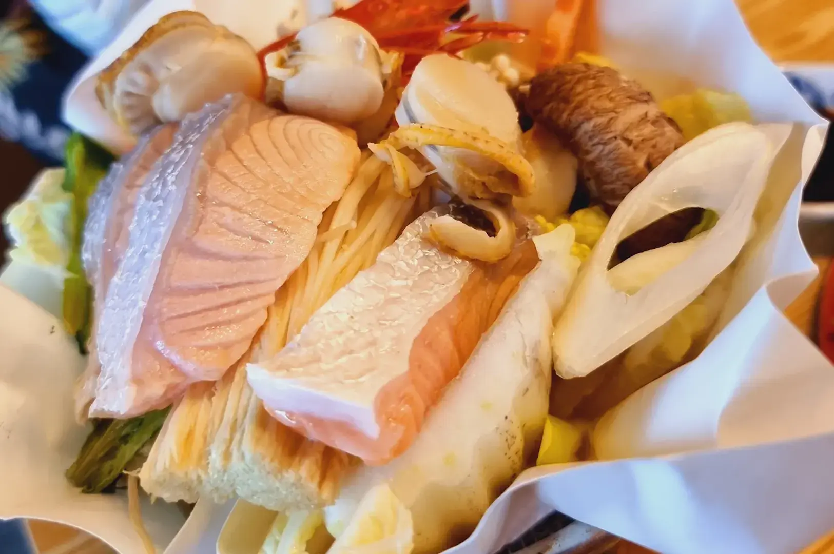 A paper-lined bowl of seafood and vegetables topped with salmon, clams, shrimp, and mushrooms.