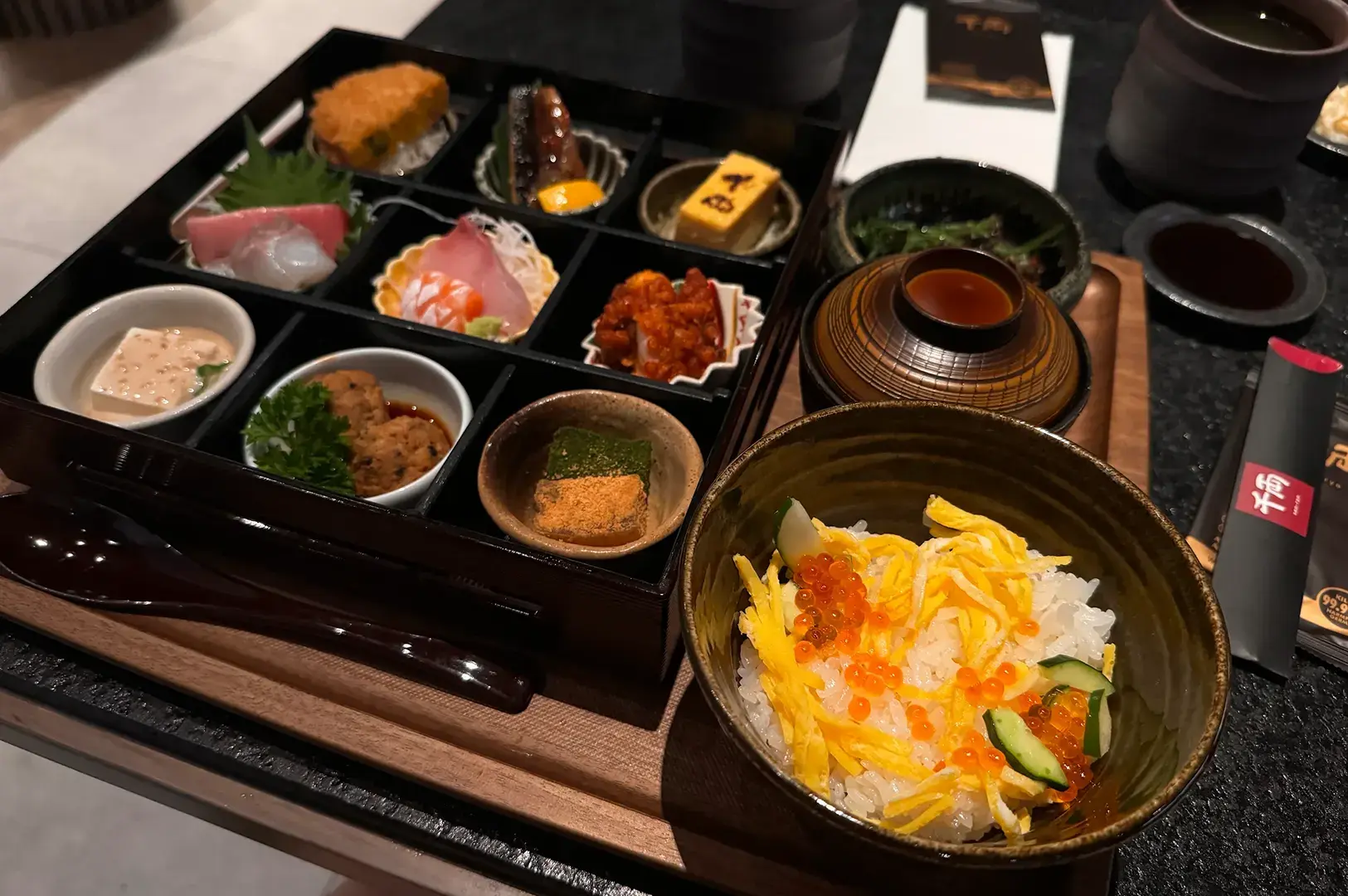 Bento box with sashimi and small dishes, chirashi bowl with salmon roe and uni.