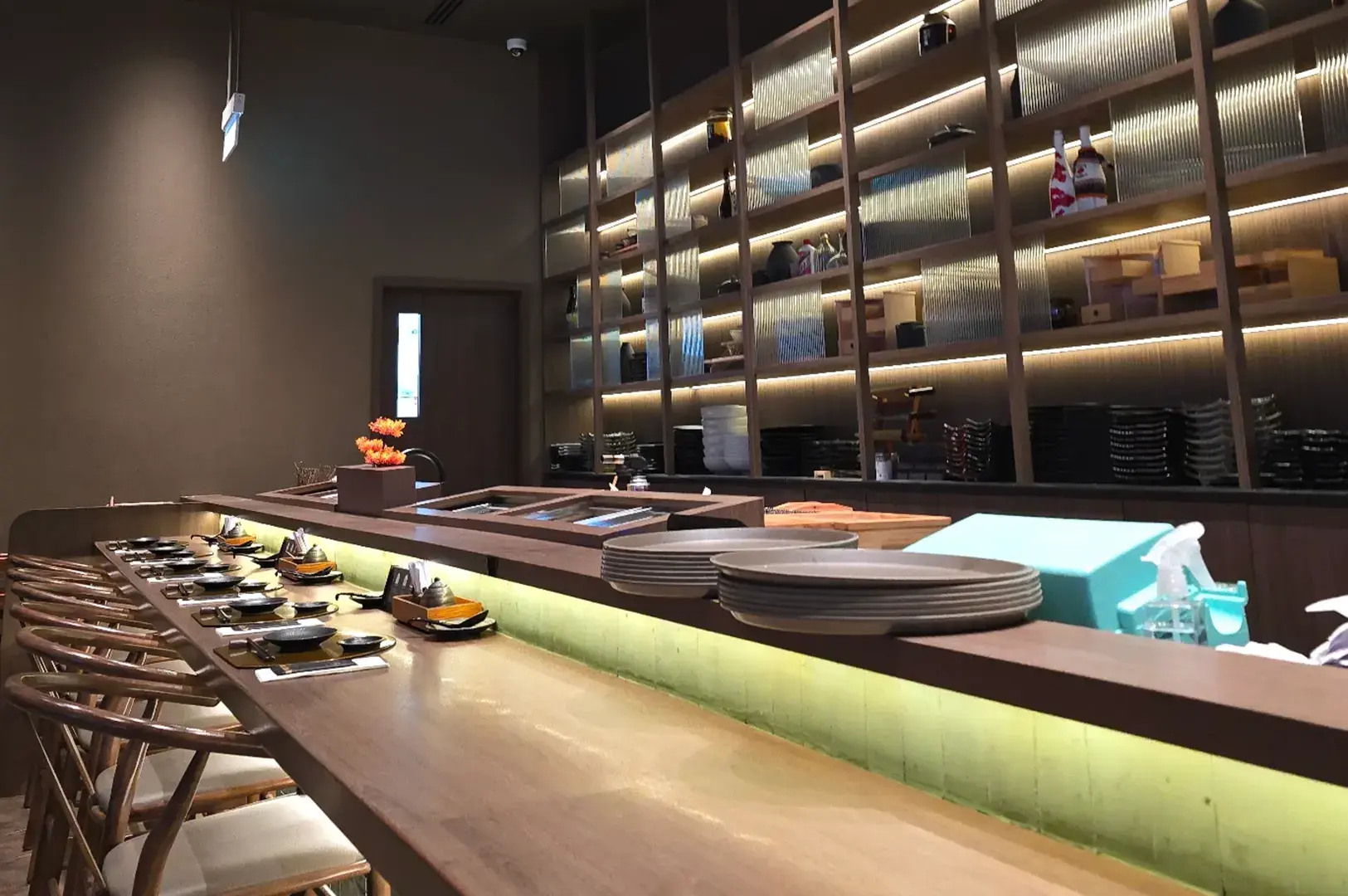 Sen-ryo sushi counter with green backlit bar and wooden stools.