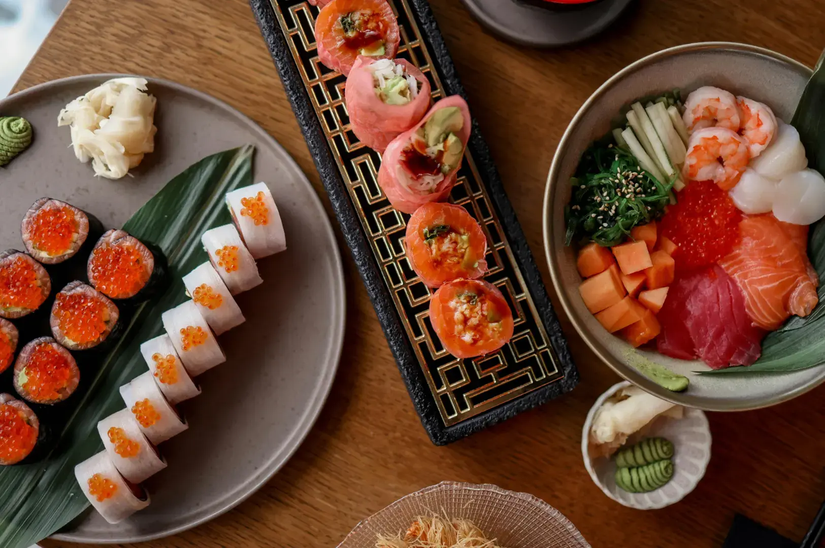Assorted sushi nigiri, salmon aburi rolls, and chirashi bowl with sashimi on wooden table