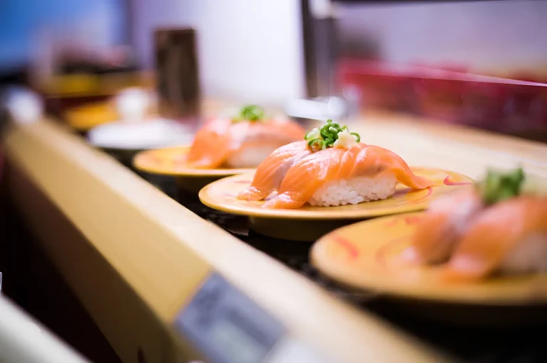 Close-up of plated salmon with herbs on small round plates, arranged along a counter with blurred background in a restaurant setting.