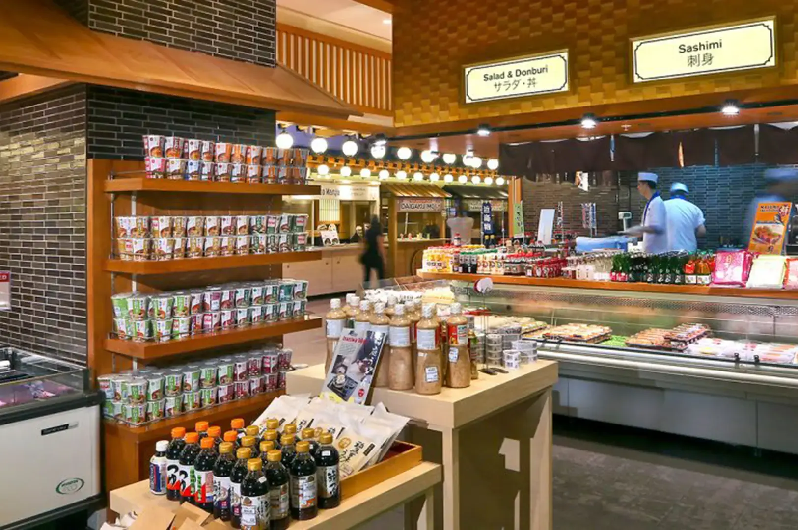 Japanese market interior with shelves of canned goods, bottled sauces, condiments, and counters for salad, donburi, and sashimi.