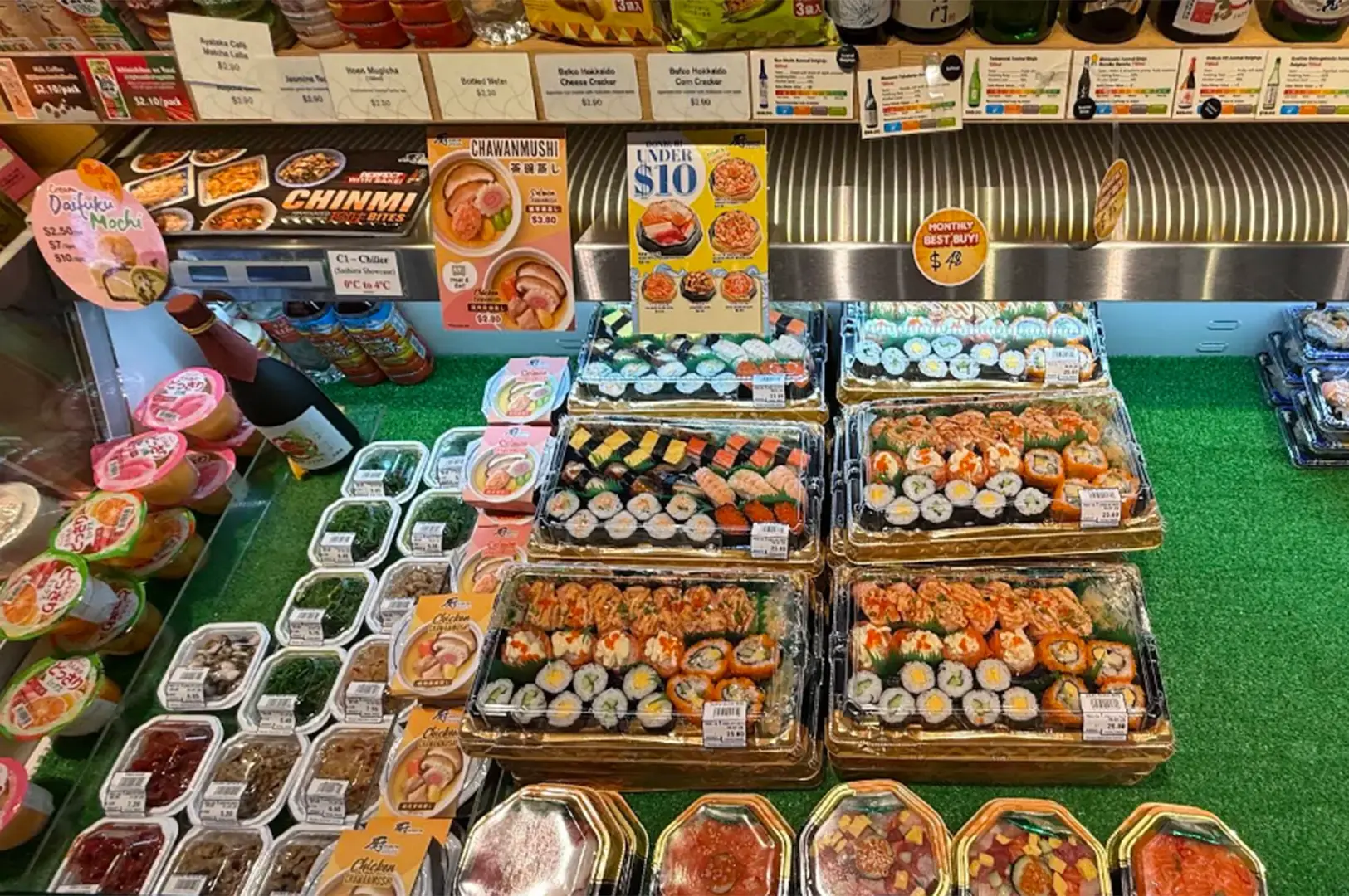 Packaged sushi, sashimi, sauces, desserts, and Japanese food products arranged in market displays.