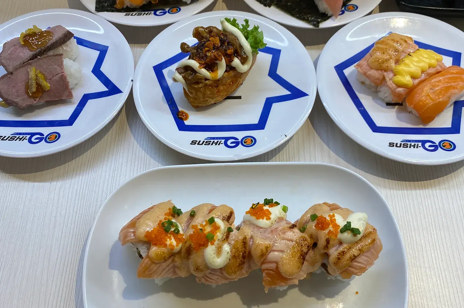 Assorted sushi on Sushi-Go plates, including seared salmon, salmon nigiri, and other toppings.