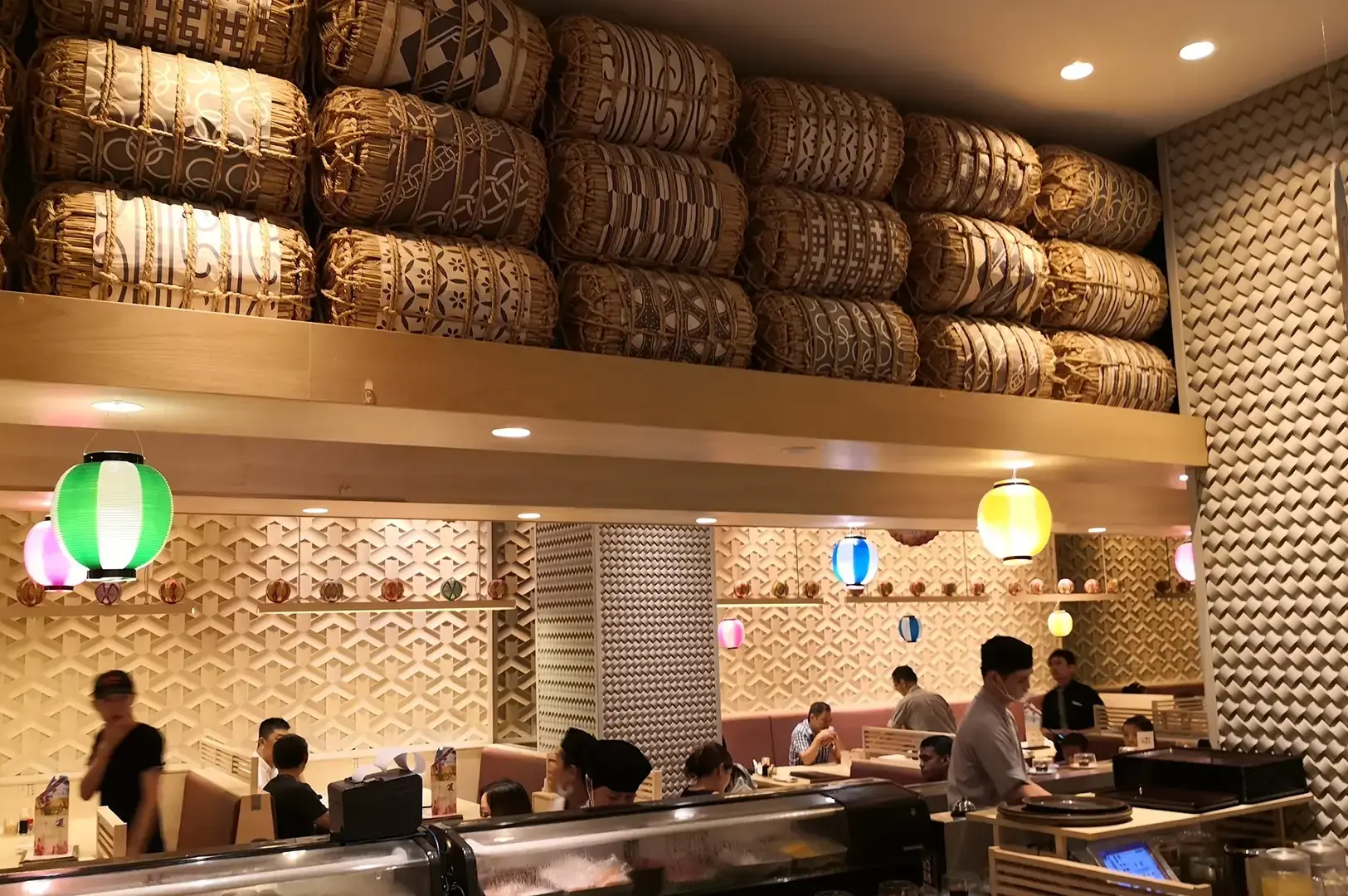 Ichiban Boshi dining area featuring stacked woven baskets, textured patterned walls, colourful pendant lights, open kitchen counters, and seated diners.