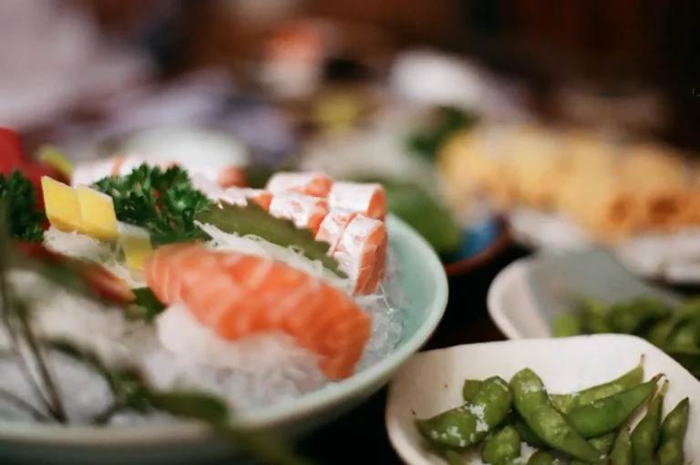 Close-up of salmon sashimi, assorted sushi, and edamame served on a dining table.