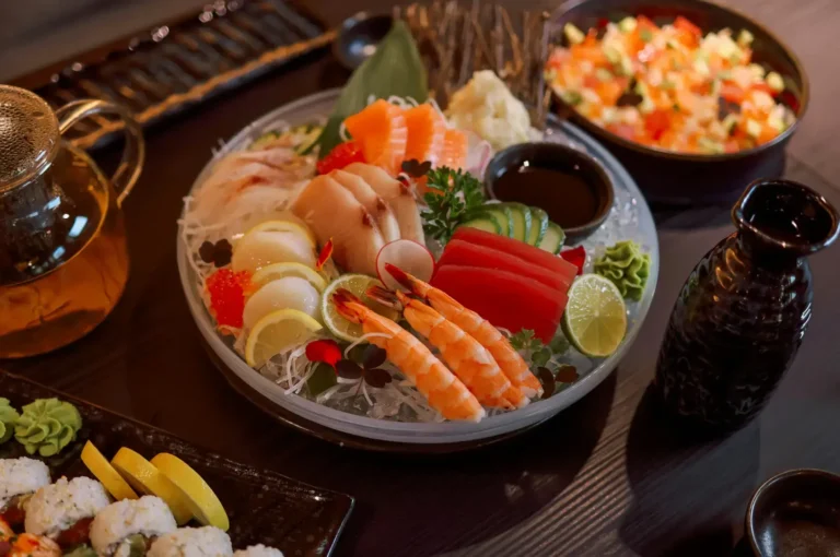 Assorted seafood platter on a wooden table, with a central bowl of shrimp and sliced fish, lemon wedges, dipping sauces, and side dishes of rice and salad.