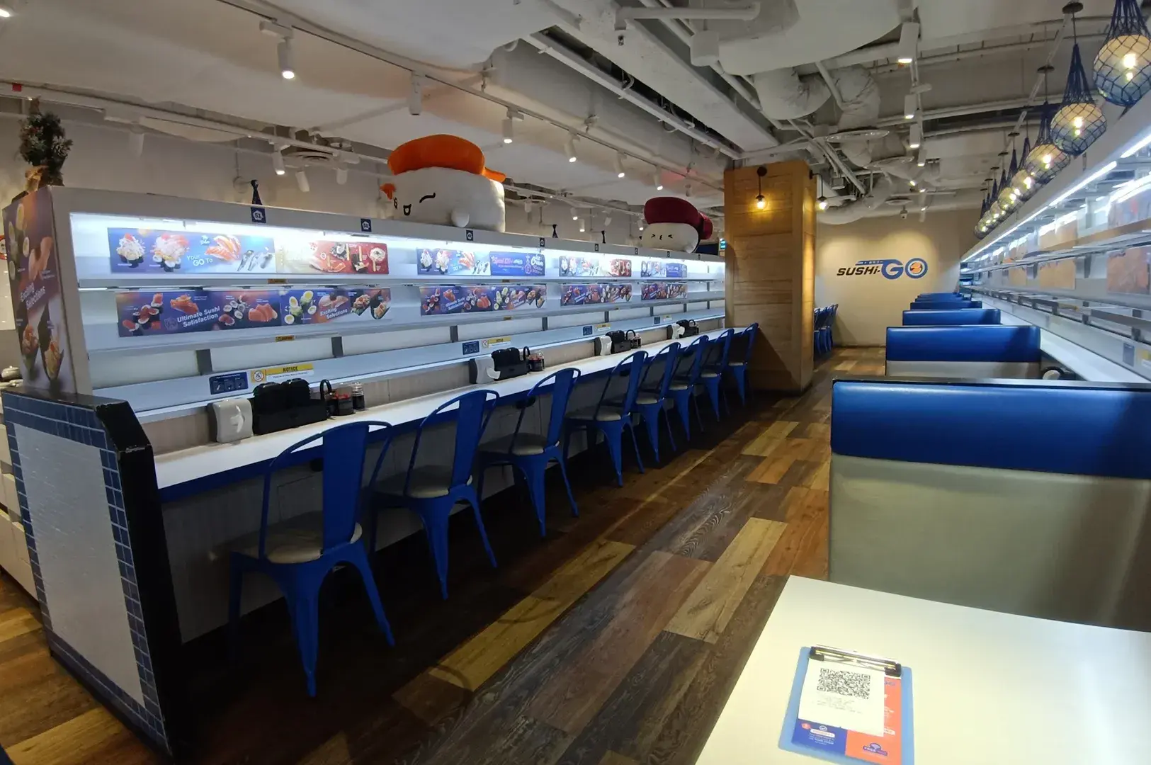 Sushi-Go interior with a conveyor belt, blue chairs, counter seating, and booth seating.