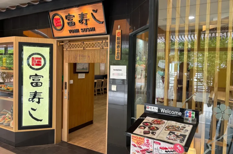 Tomi Sushi entrance at Millenia Walk with illuminated Japanese signage, a traditional noren curtain, glass windows, a welcome board, and menu displays outside the doorway.