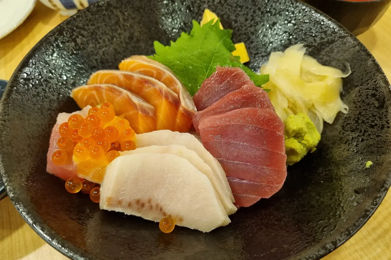 Delicious chirashi don rice bowl topped with fresh salmon slices, tuna sashimi, and bright orange fish roe in a black ceramic bowl.