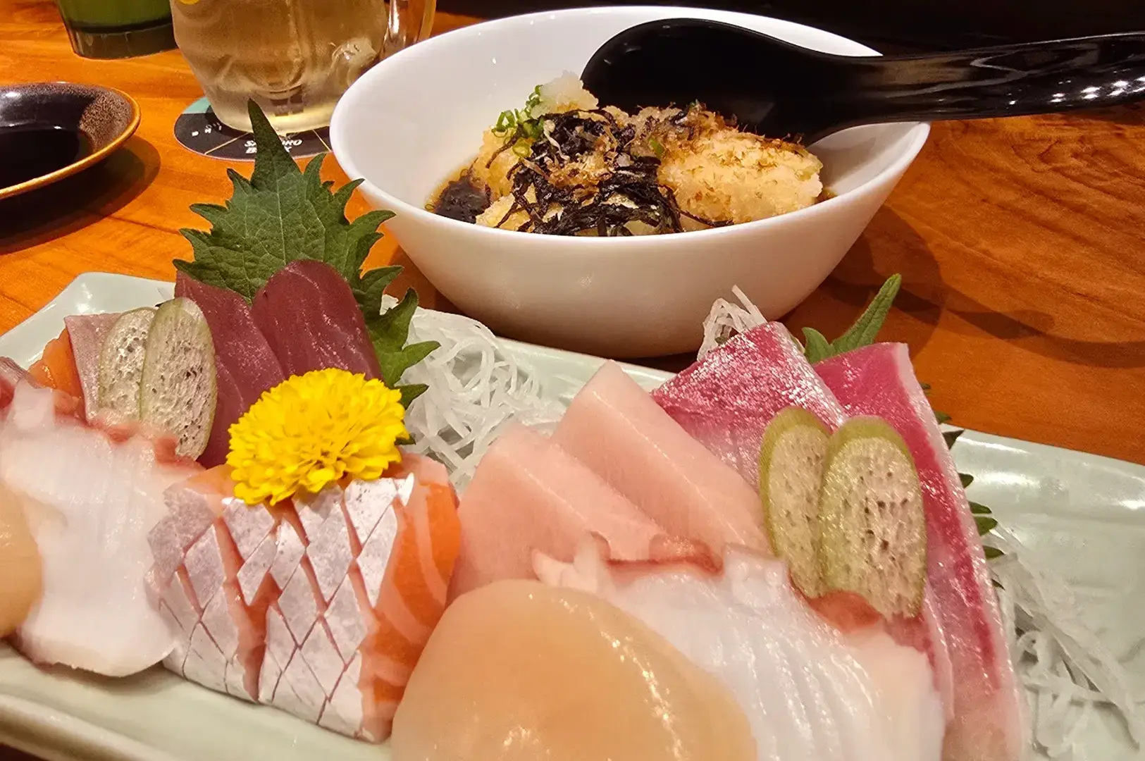 Assorted sashimi platter with tuna, salmon, white fish, shiso leaves, shredded daikon, and a yellow chrysanthemum beside a bowl of rice.