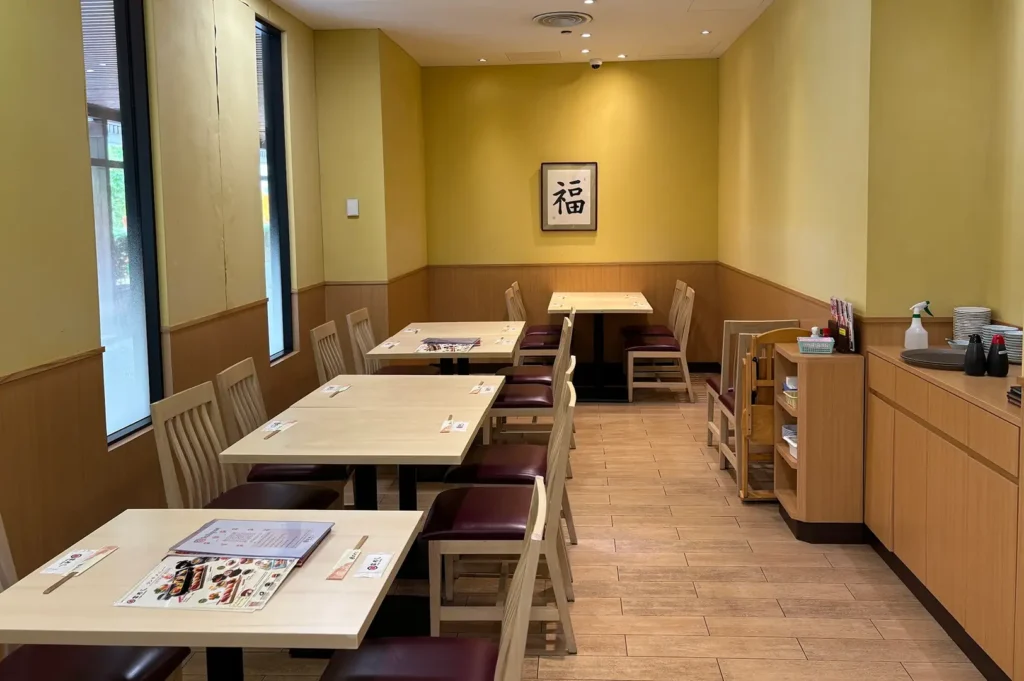 Empty Tomi Sushi dining room at Millenia Walk with neatly arranged wooden tables, chairs, menus, warm yellow walls, wood-panelled accents, and a framed Japanese character artwork.