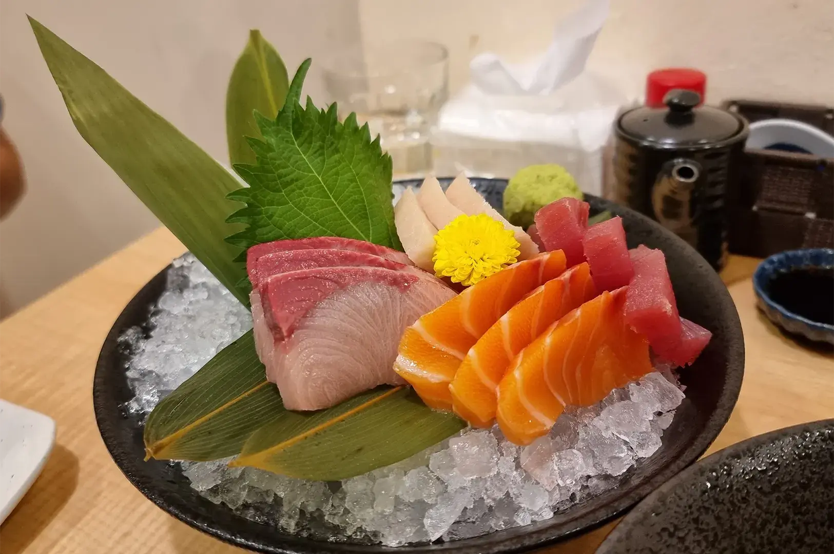 Fresh assorted Japanese sashimi platter featuring salmon, tuna, and white fish served on a bed of ice with shiso leaf and garnish.
